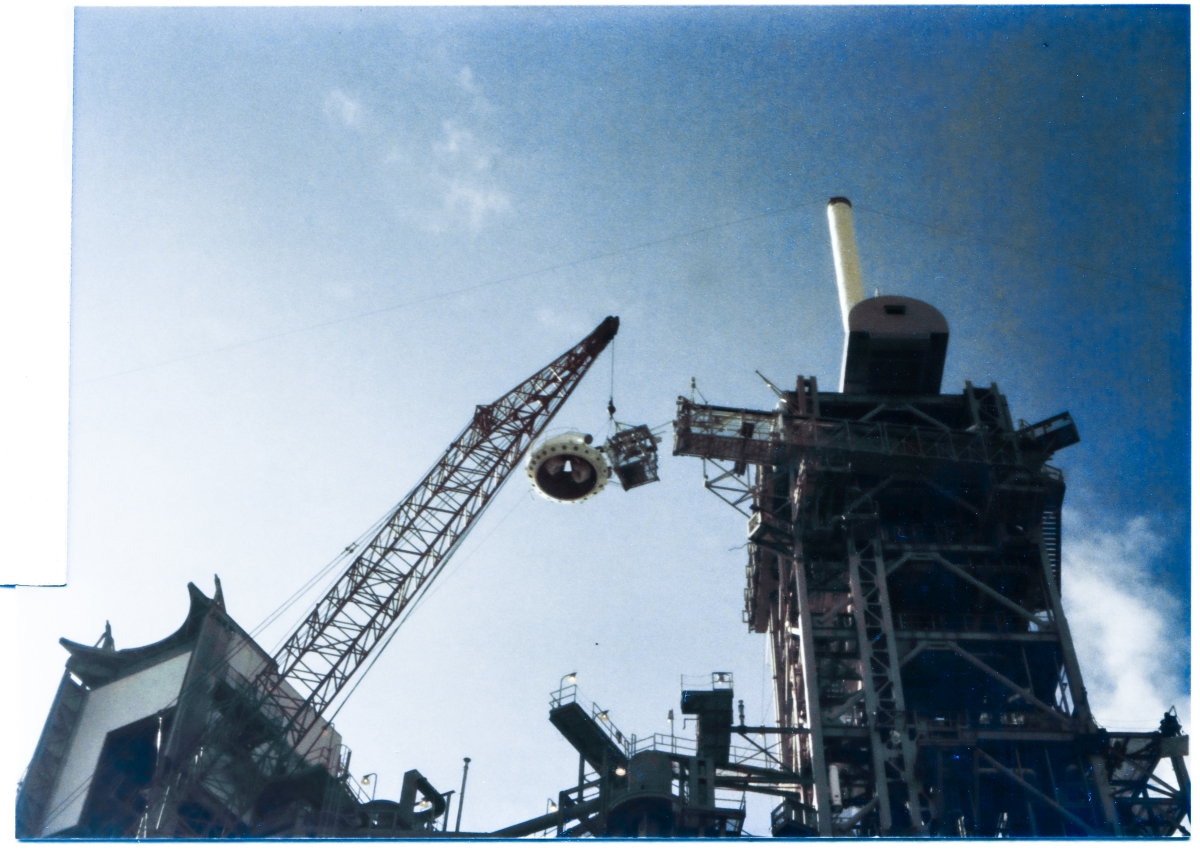 Image 120. The Gaseous Oxygen Vent System Tip Assembly has been lifted high above the Pad Deck at Space Shuttle Launch Complex 39-B, Kennedy Space Center, Florida, where it is about to be bolted on to the end of the GOX Arm by Union Ironworkers working for Ivey Steel. The Arm is in its retracted position, folded back against the Fixed Service Structure which it is attached to via a system of Hinges which allow it to be extended outward, taking the Vent Hood, which is part of the Tip Assembly, and placing it over the top of the Space Shuttle's External Tank where it can be employed in the collection, warming, diluting, and ducting-away of the exceptionally-cold Gaseous Oxygen which is released by the External Tank when it is filled up with Liquid Oxygen. Photo by James MacLaren.